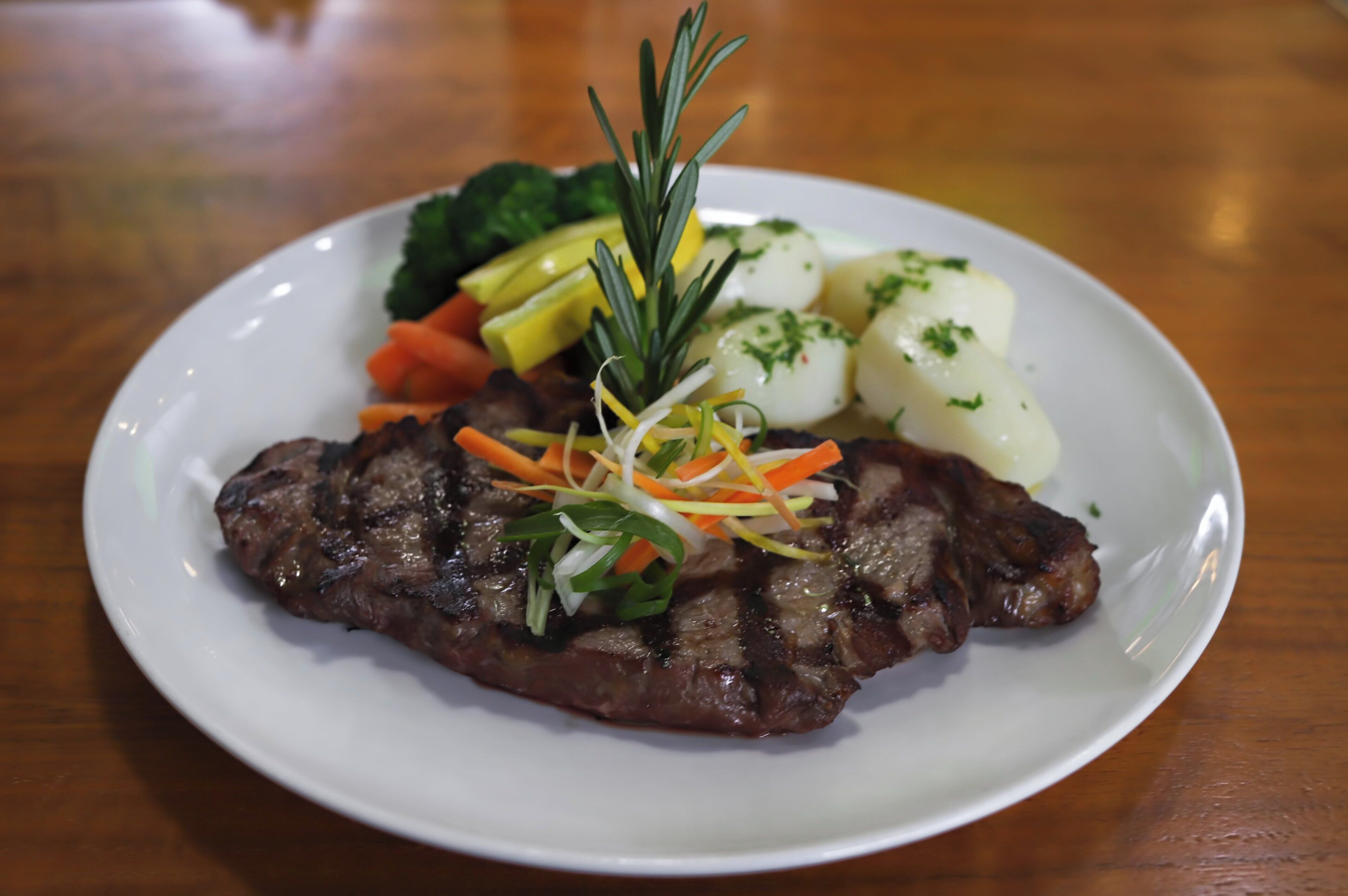 Un plato con bistec, verduras y una ramita de romero.