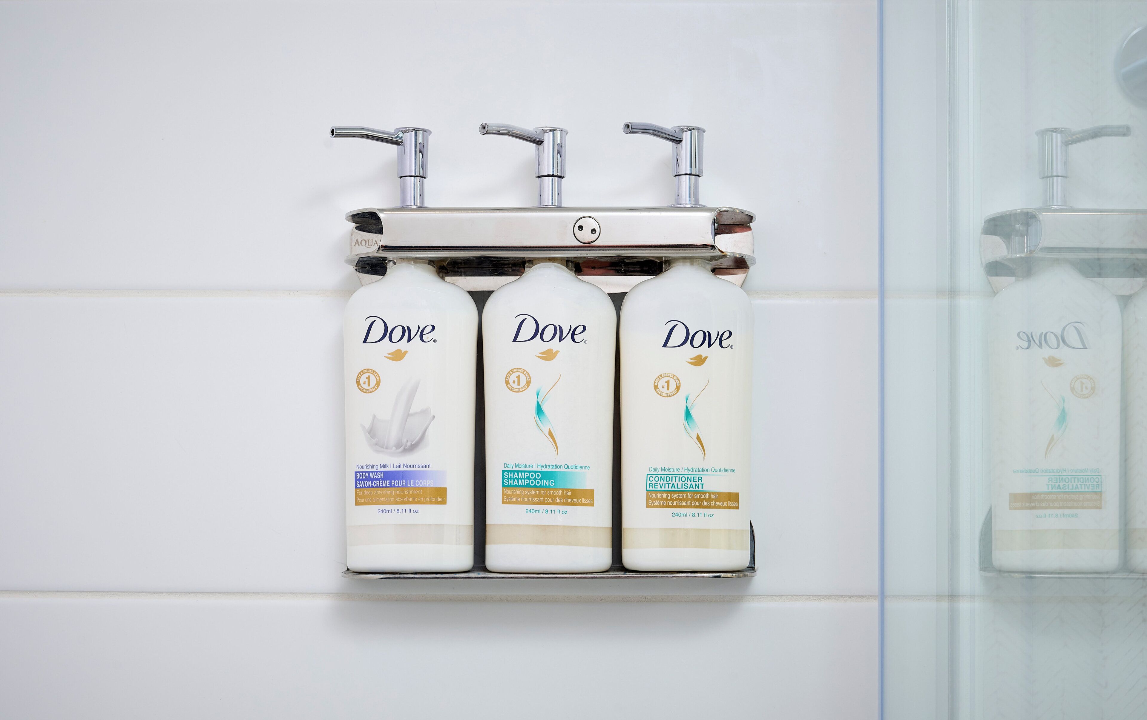Trois produits de la gamme Dove pour les soins personnels, présentés sur un distributeur mural.