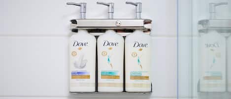 Three Dove personal care products mounted on a wall-mounted dispenser.