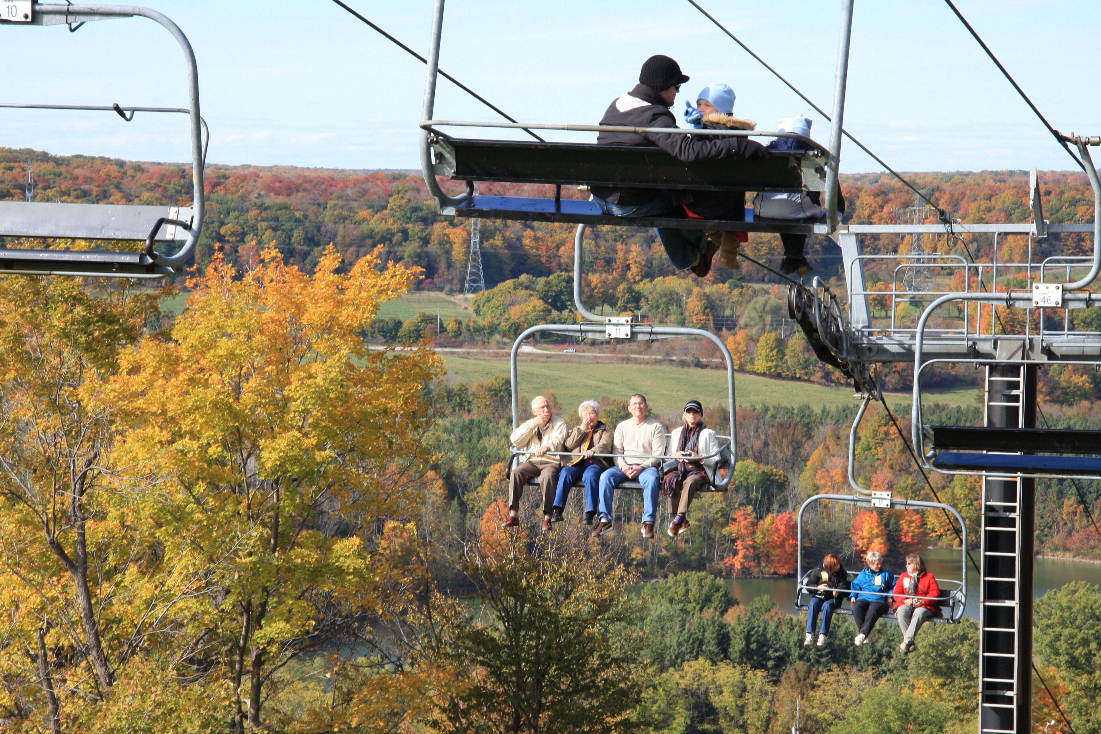 A cable car with passengers enjoying a scenic view of autumn foliage and a lake.