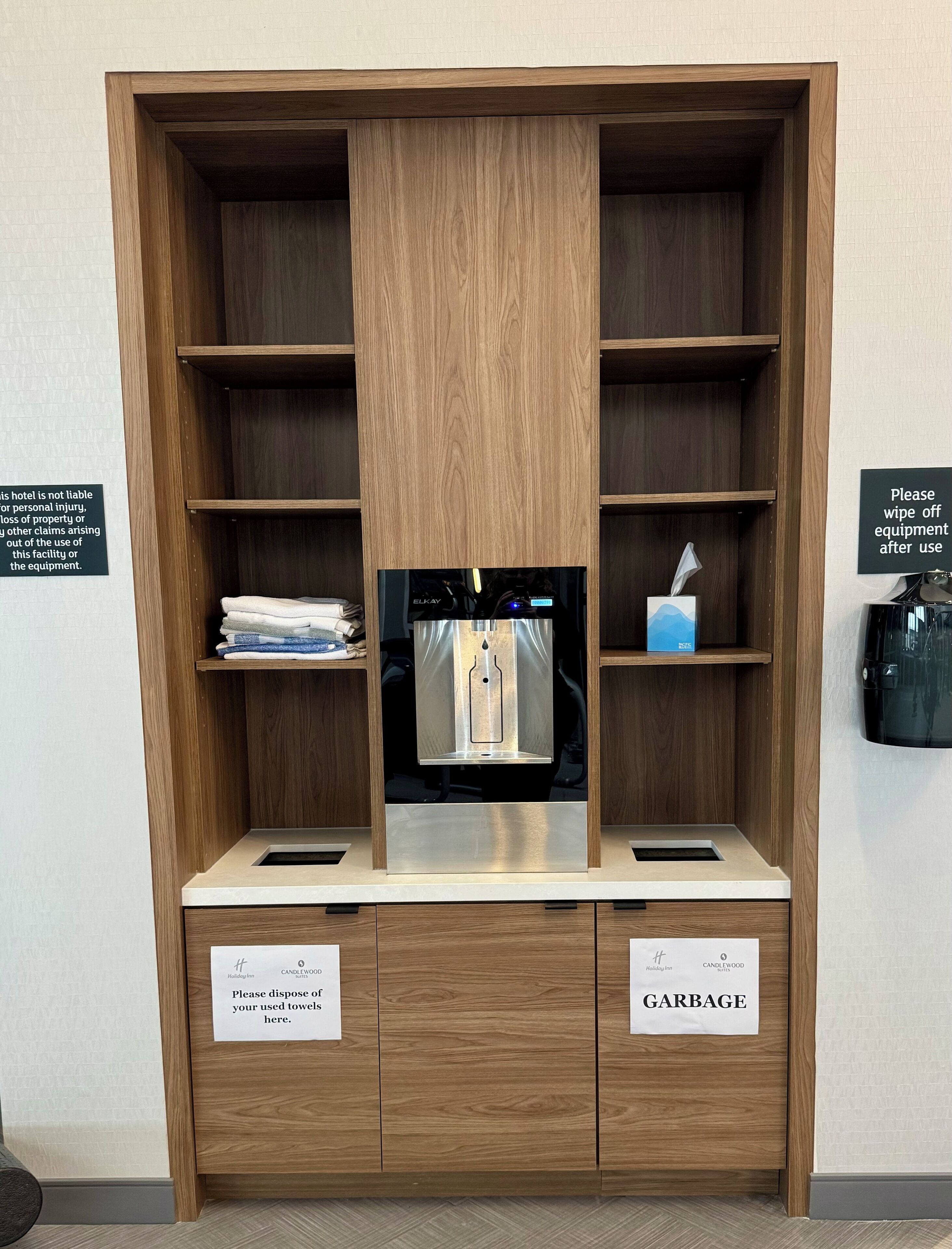 Une chambre d’hôtel équipée d’un meuble en bois contenant un mini-bar, un distributeur de serviettes et une poubelle. Des panneaux indiquent où jeter les serviettes et les déchets.