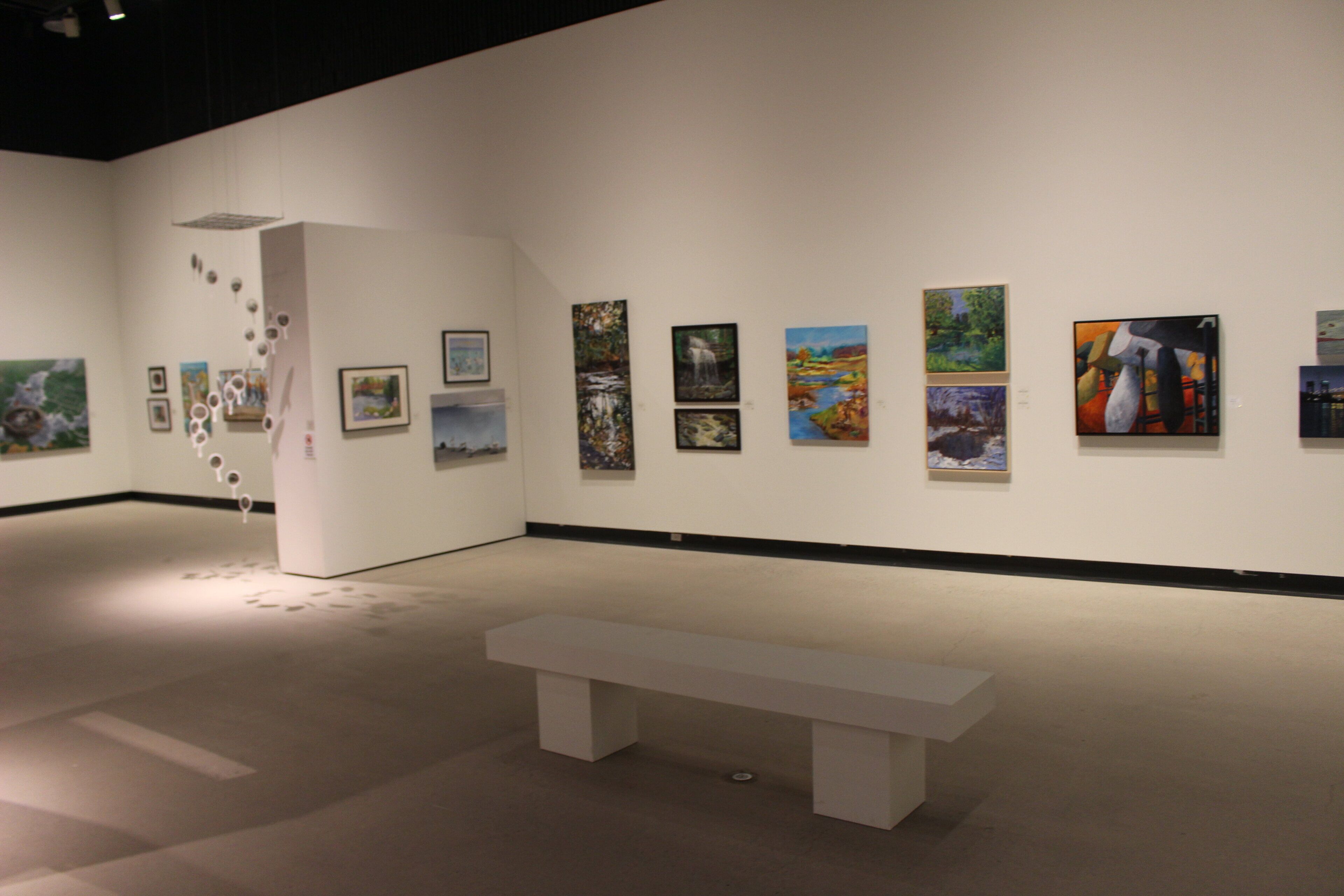 An art gallery with paintings on the walls and a white bench in the center.