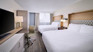 A hotel room with two beds, a TV, a desk with a lamp, and a chair.