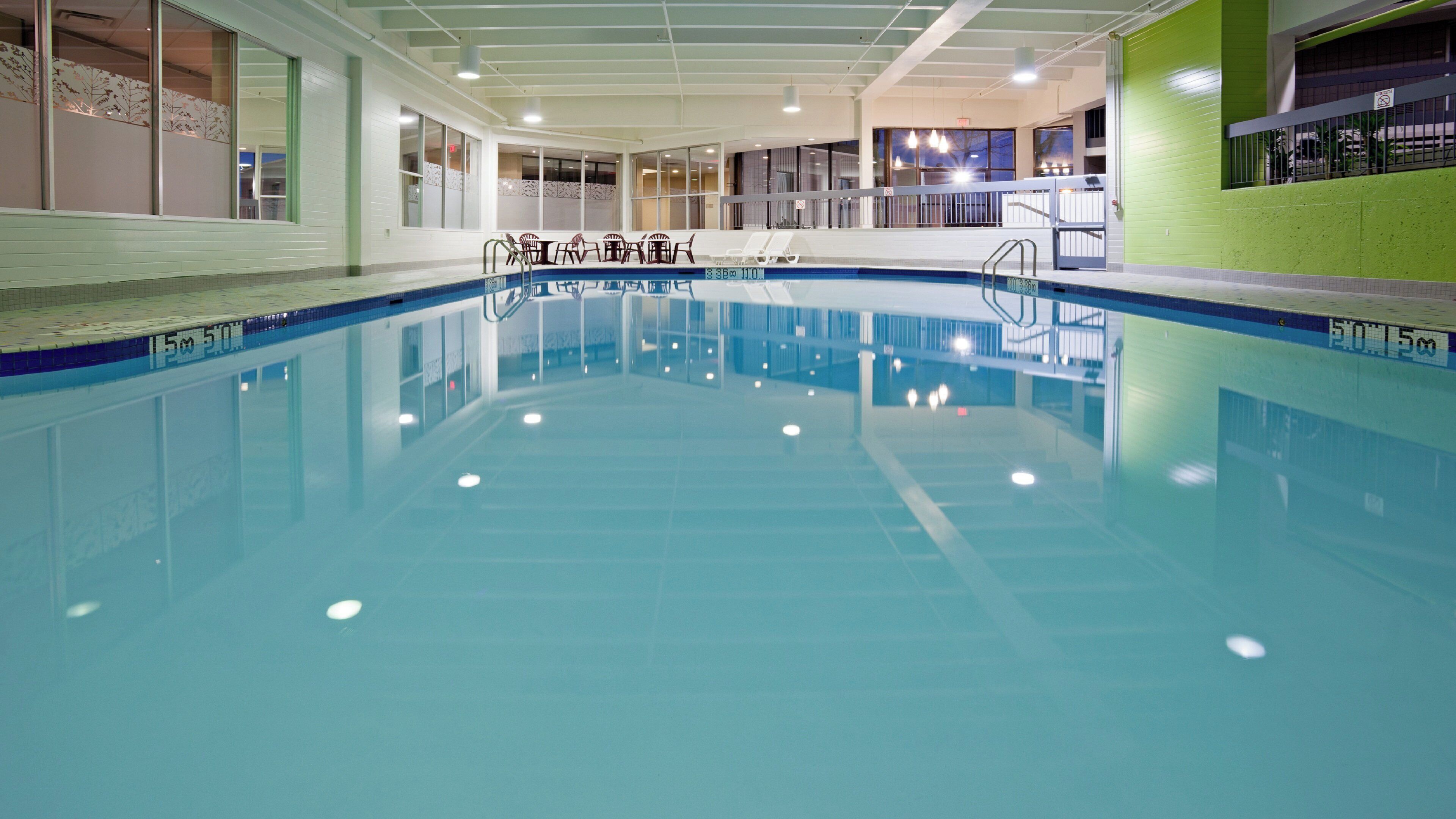 Una piscina interior con agua cristalina, un trampolín y una zona de estar con sillas.