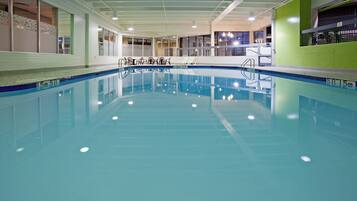 Una piscina interior con agua cristalina, un trampolín y una zona de estar con sillas.