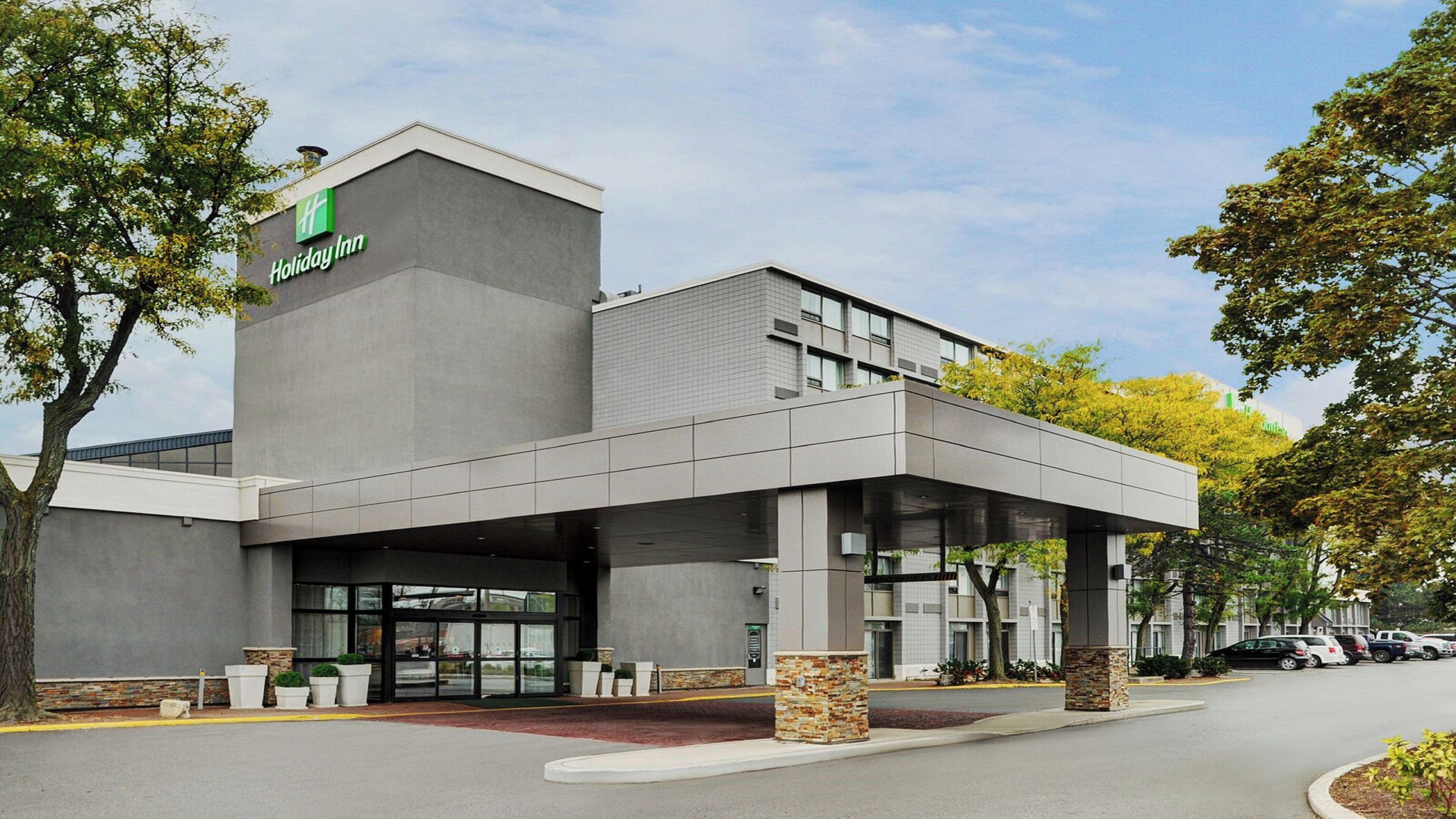 A Holiday Inn hotel with a modern design, featuring a covered entrance and a parking lot.