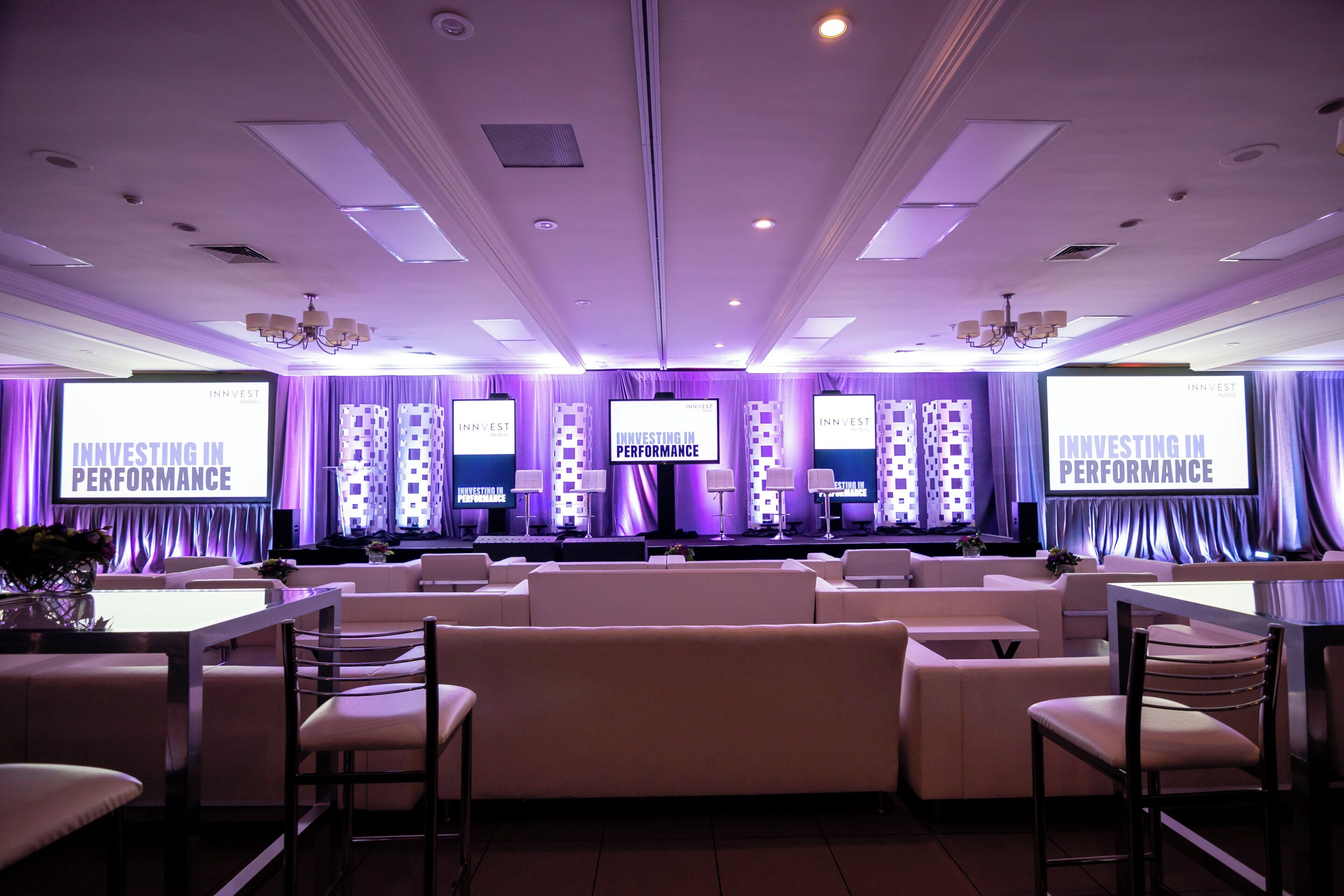 A conference room with multiple screens displaying 'Investing in Performance' and a stage with a backdrop.
