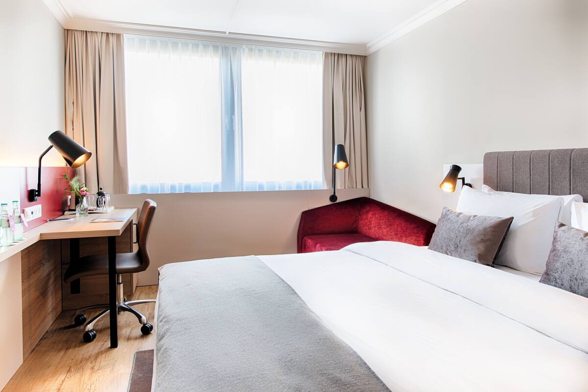 A hotel room with a bed, desk, chair, and two lamps.