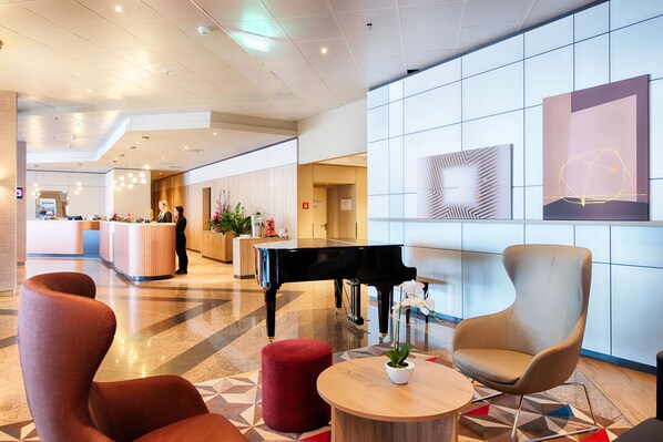 Un lobby moderno con una recepción, un piano de cola, asientos cómodos y un ventanal con arte mural geométrico.