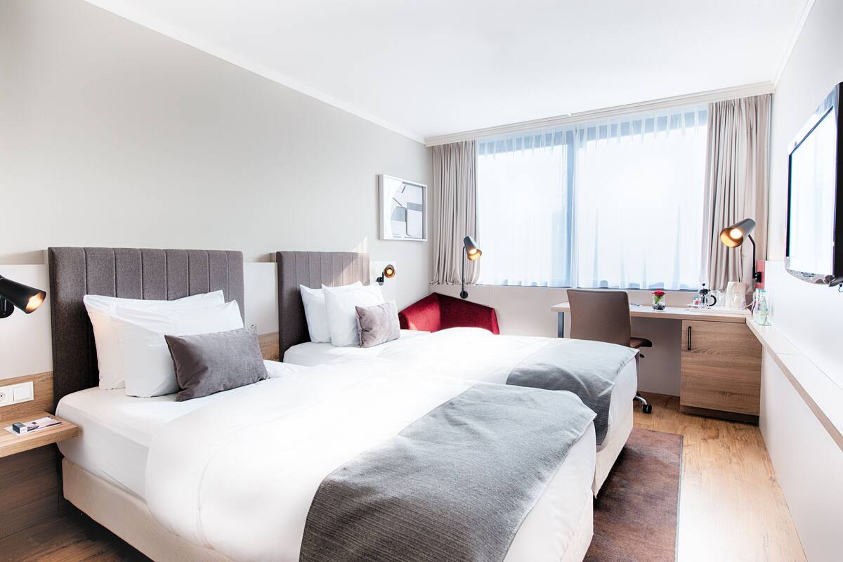 A hotel room with two beds, a desk, and a chair.