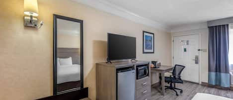 A hotel room with a bed, a desk with a computer, a refrigerator, a microwave, a chair, and a television.