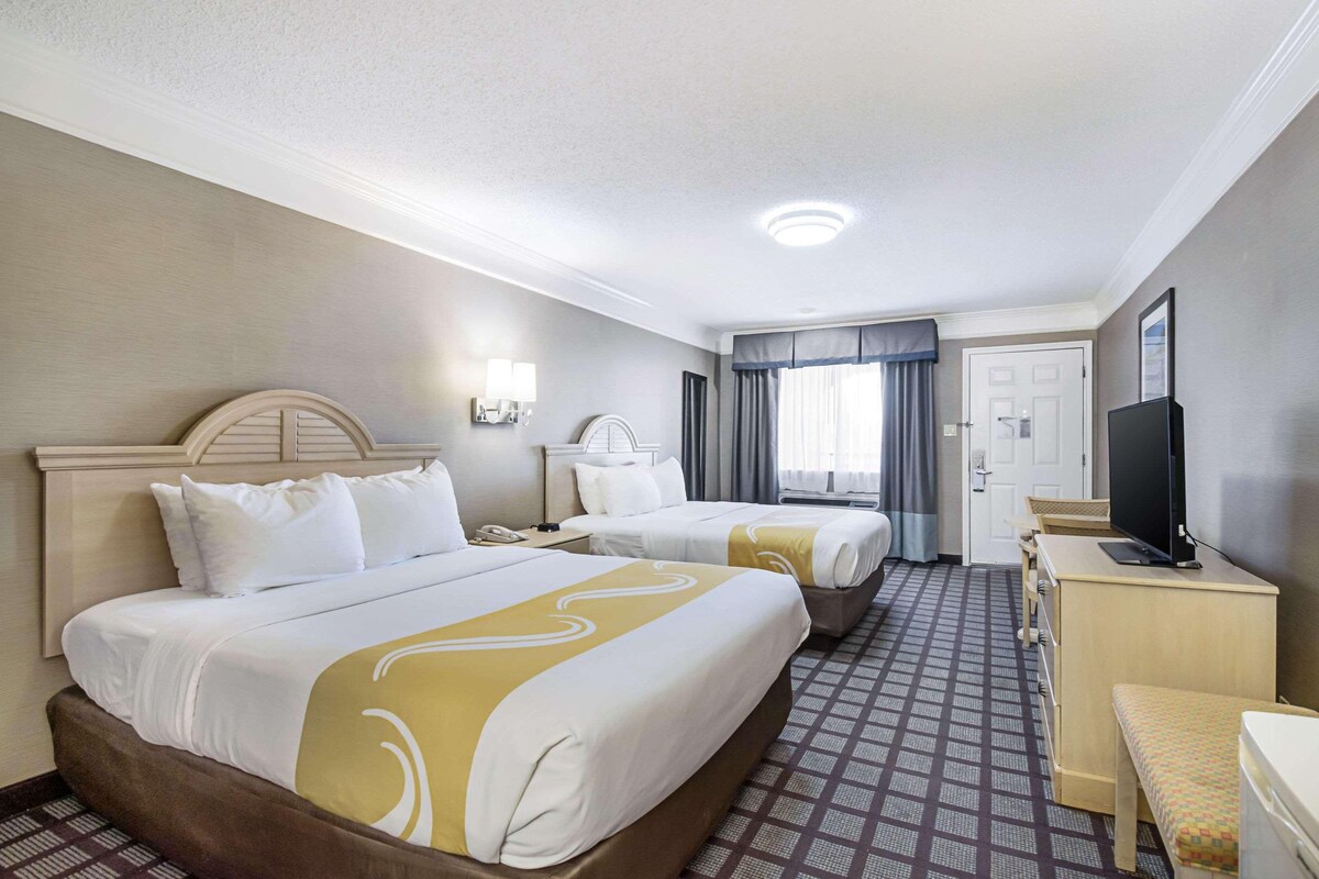 A hotel room with two beds, a desk, a television, and a door.