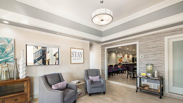 A spacious living area with a grey armchair, a small side table, and a decorative cabinet. A staircase is visible in the background leading to a dining area. - Quality Inn Near Lake Marble Falls (Marble Falls)