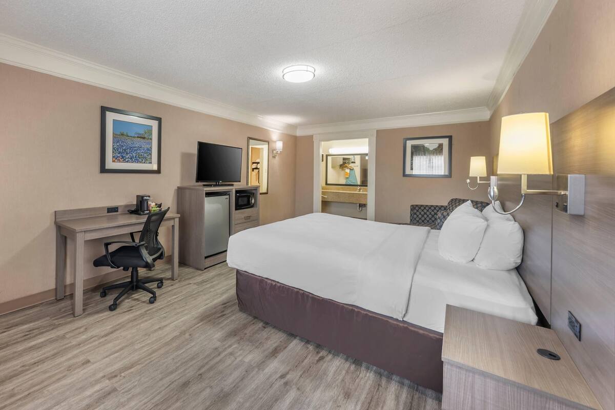 Une chambre d’hôtel équipée d’un lit, d’un bureau, d’une chaise, d’une télévision et d’une salle de bain visible à travers une porte ouverte.