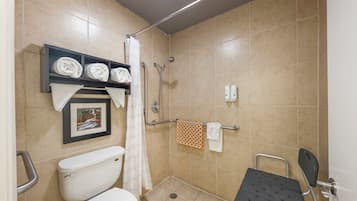 Un baño pequeño y limpio con inodoro, ducha con barra de apoyo, estante con toallas y un cuadro en la pared.
