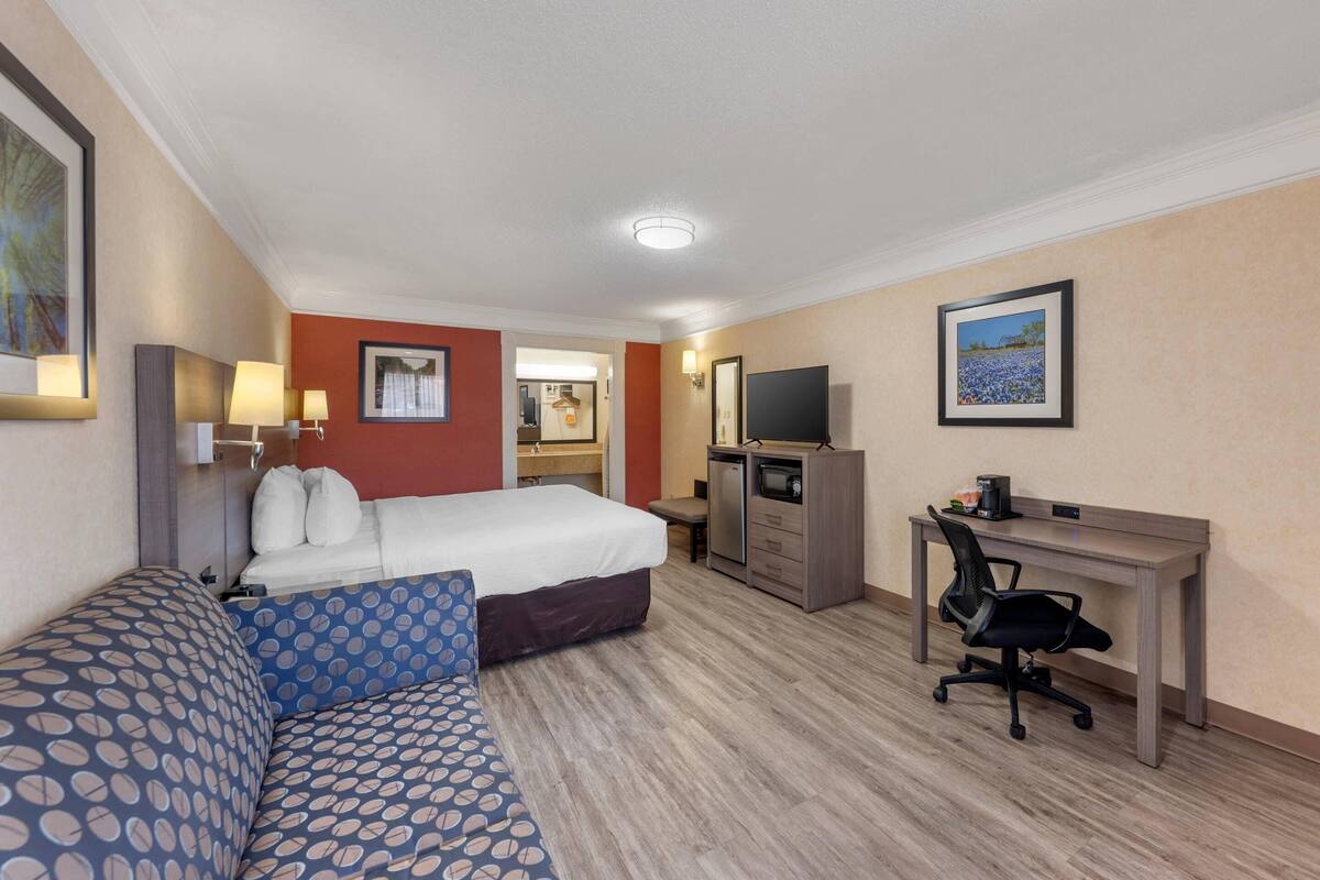 Une chambre d’hôtel équipée d’un lit, d’un canapé, d’un bureau, d’une chaise, d’une télévision et d’une petite kitchenette.