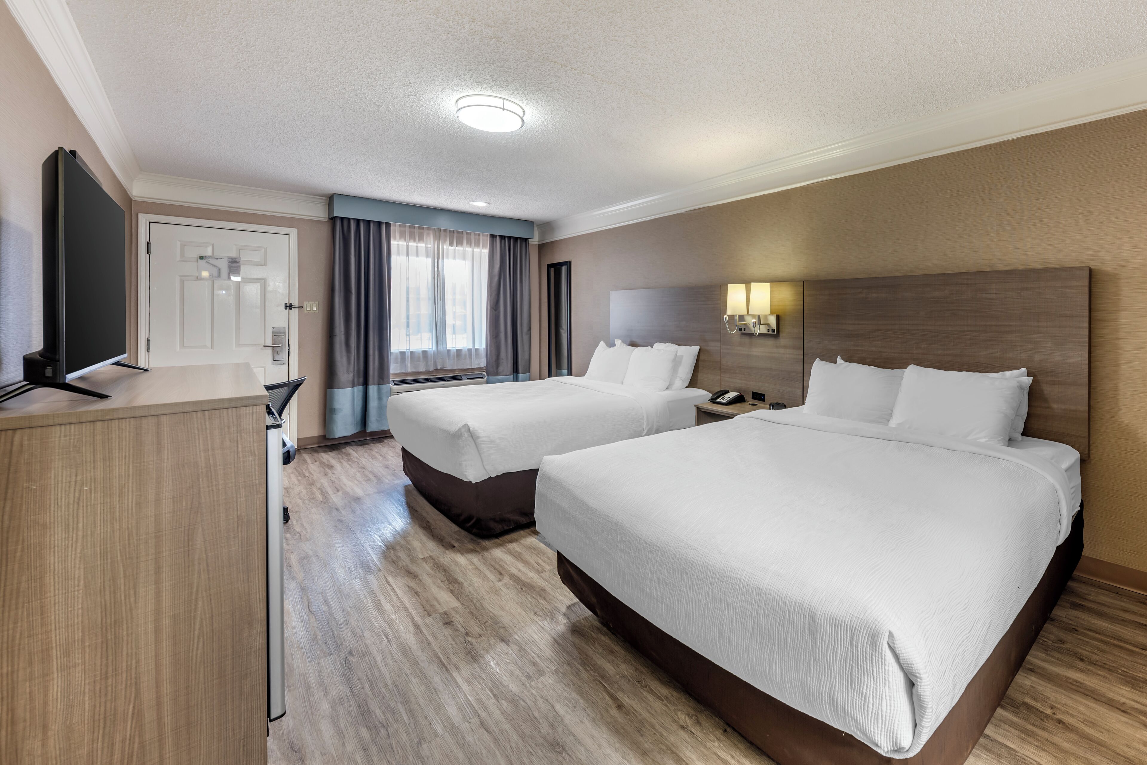Habitación de hotel con dos camas, un escritorio, un televisor y una ventana con cortinas.
