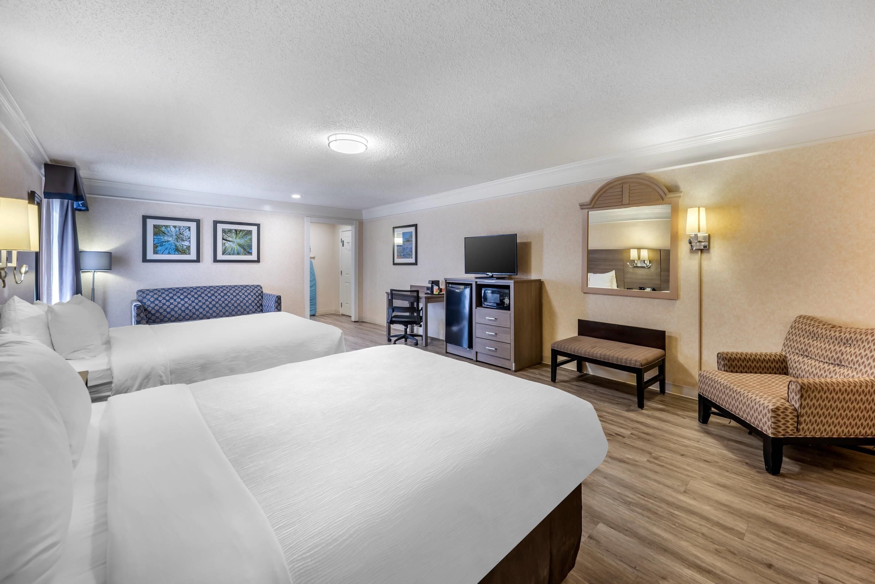 A hotel room with two beds, a desk with a computer, a TV, a chair, and a mirror.