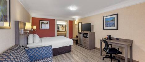 A hotel room with a bed, a desk, a chair, a TV, and a painting on the wall.