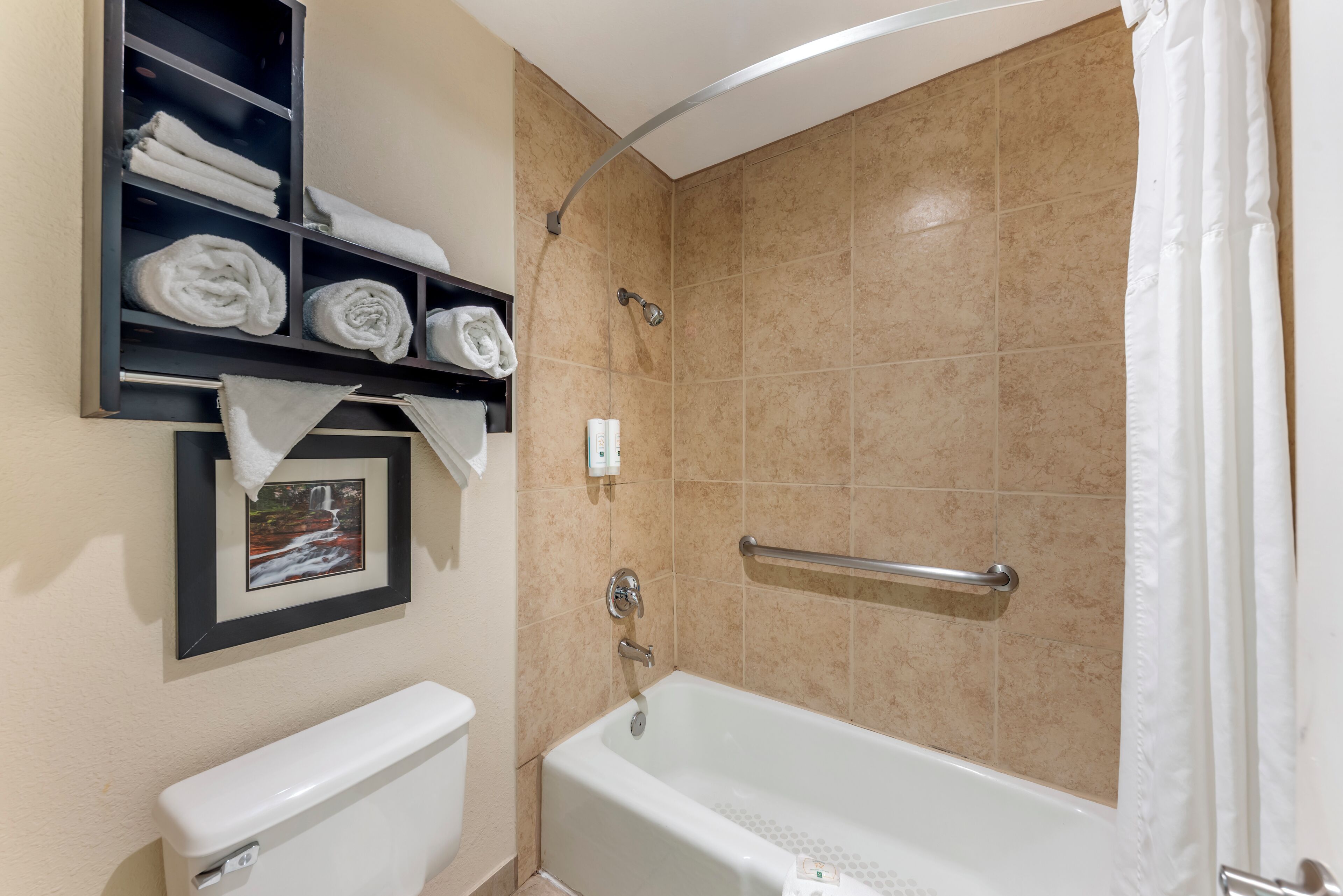 A bathroom with a bathtub, a toilet, a towel rack with towels, and a shower curtain.