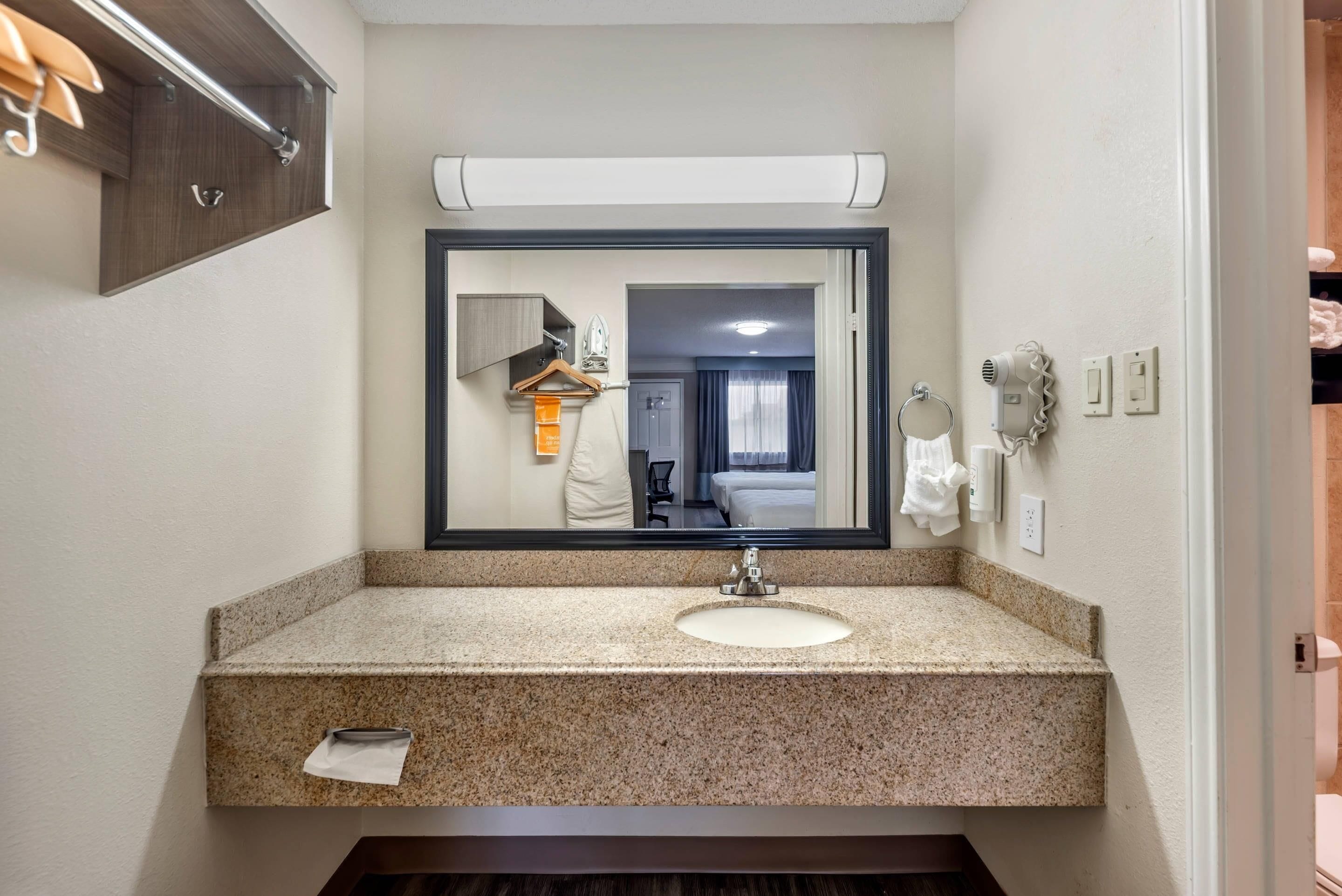 Une salle de bain moderne avec un comptoir en granit, un lavabo, un miroir, un porte-serviettes et un sèche-cheveux.