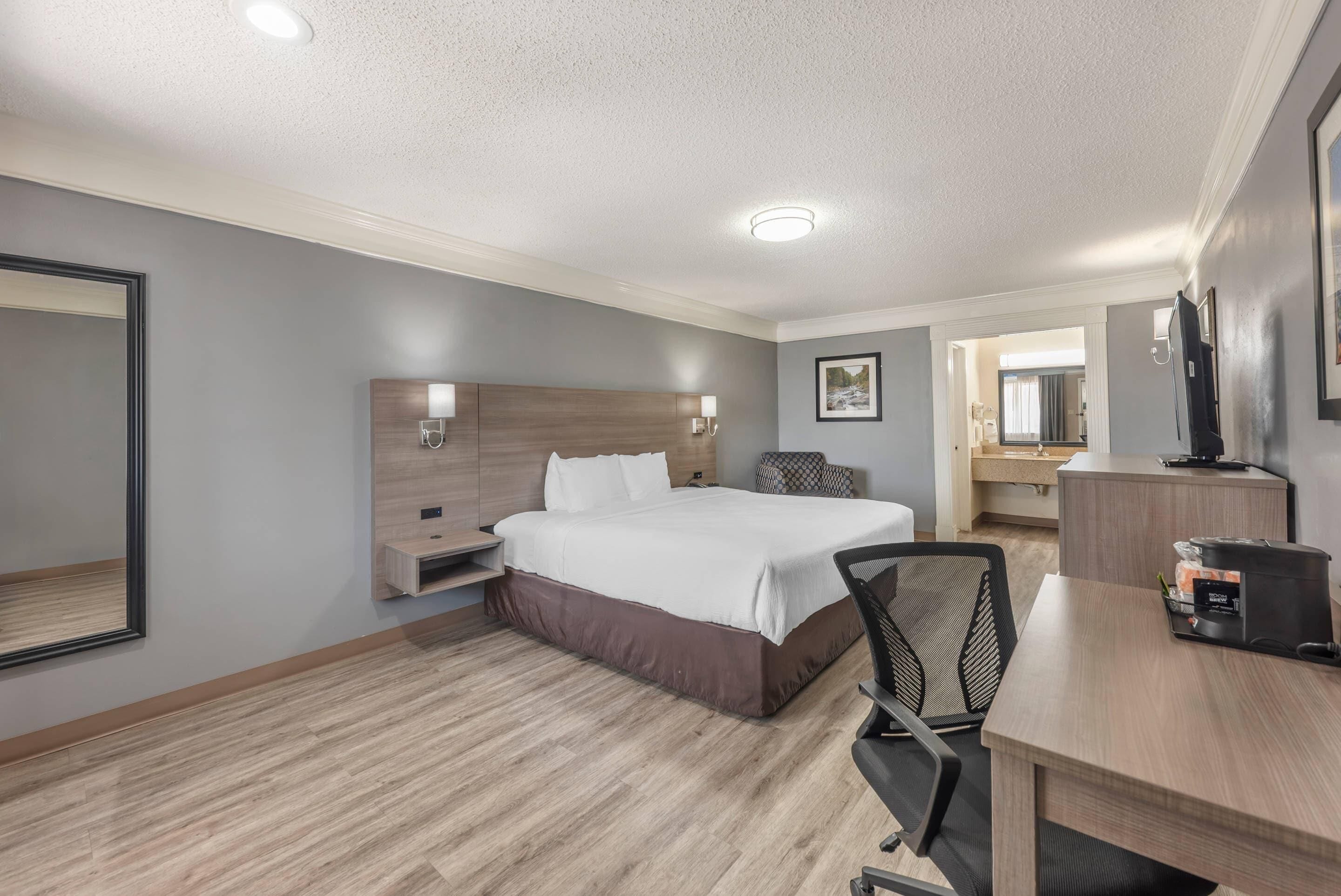 A hotel room with a bed, bedside tables, a desk, a chair, and a mirror.