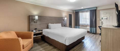 A hotel room with a large bed, a sofa, a desk, and a TV.