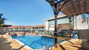 A swimming pool area with a covered seating area and a building in the background. - Quality Inn Near Lake Marble Falls (Marble Falls)