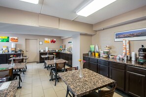 A hotel kitchen with granite countertops, dining tables, chairs, and a coffee machine. - Quality Inn near Potomac Mills (Woodbridge)