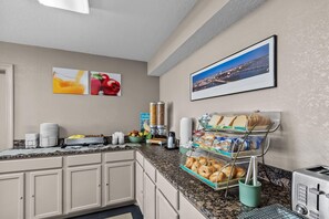 A hotel breakfast area with a coffee machine, a fruit bowl, and a bread display.