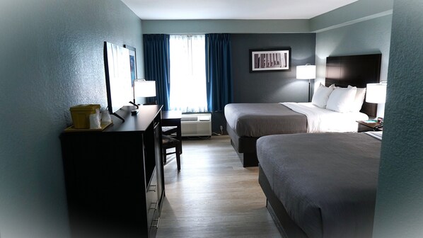 A hotel room with two beds, a desk, a chair, a lamp, and a window with curtains. - Quality Inn near Potomac Mills (Woodbridge)