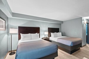 Habitación de hotel con dos camas, una mesita de noche, una lámpara y un cuadro en la pared.