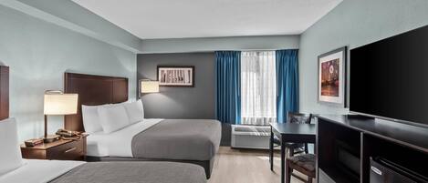 A hotel room with two beds, a desk, a television, and a window with curtains.