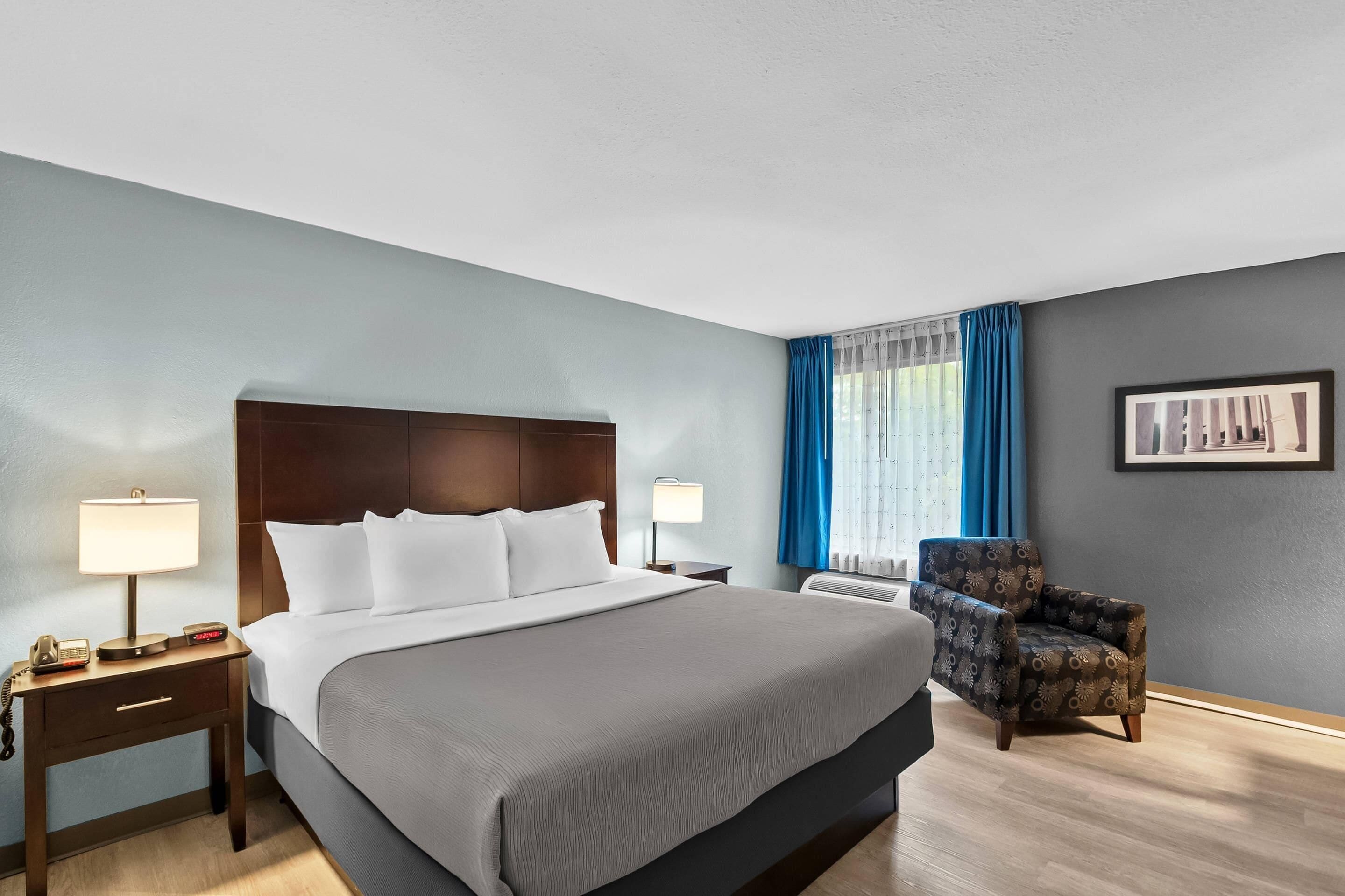 A hotel room with a large bed, bedside tables, a chair, and a picture on the wall.
