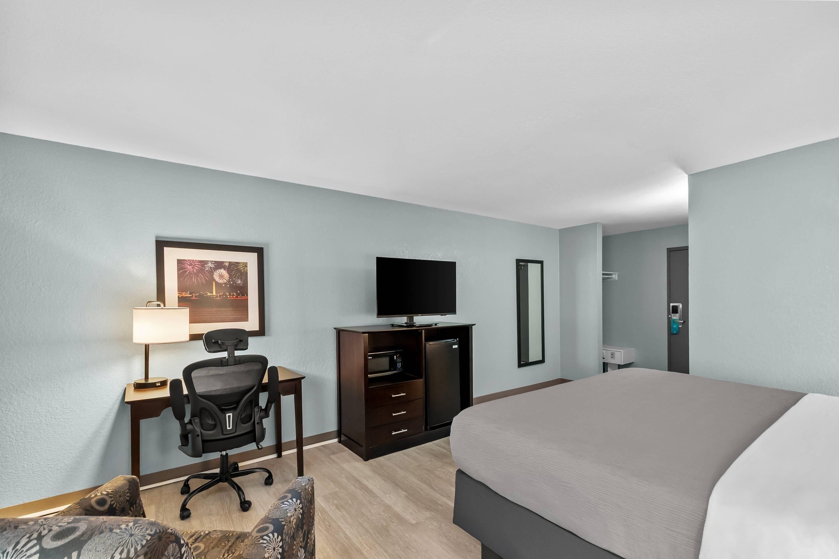 A hotel room with a bed, a desk with a chair, a television, a microwave, and a mirror.