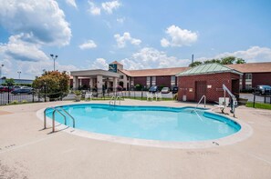 A swimming pool with a brick building in the background, a covered area with a sign, and a fenced parking area. - Quality Inn near Potomac Mills (Woodbridge)