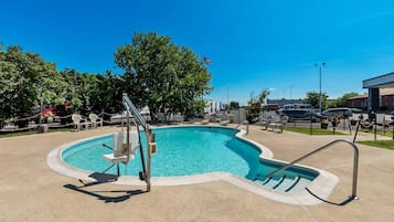 A swimming pool with a diving board, surrounded by lounge chairs and a fence.