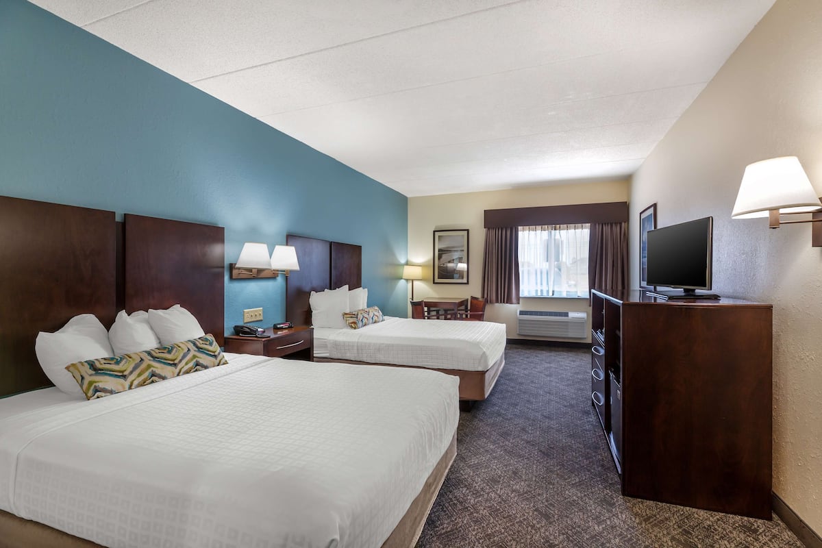 A hotel room with two beds, a desk, a television, and a desk lamp.