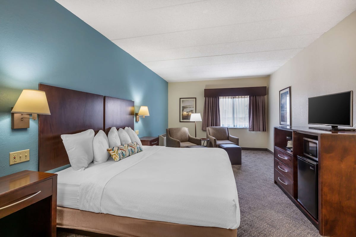 A hotel room with a large bed, two armchairs, a desk with a TV, and a dresser.