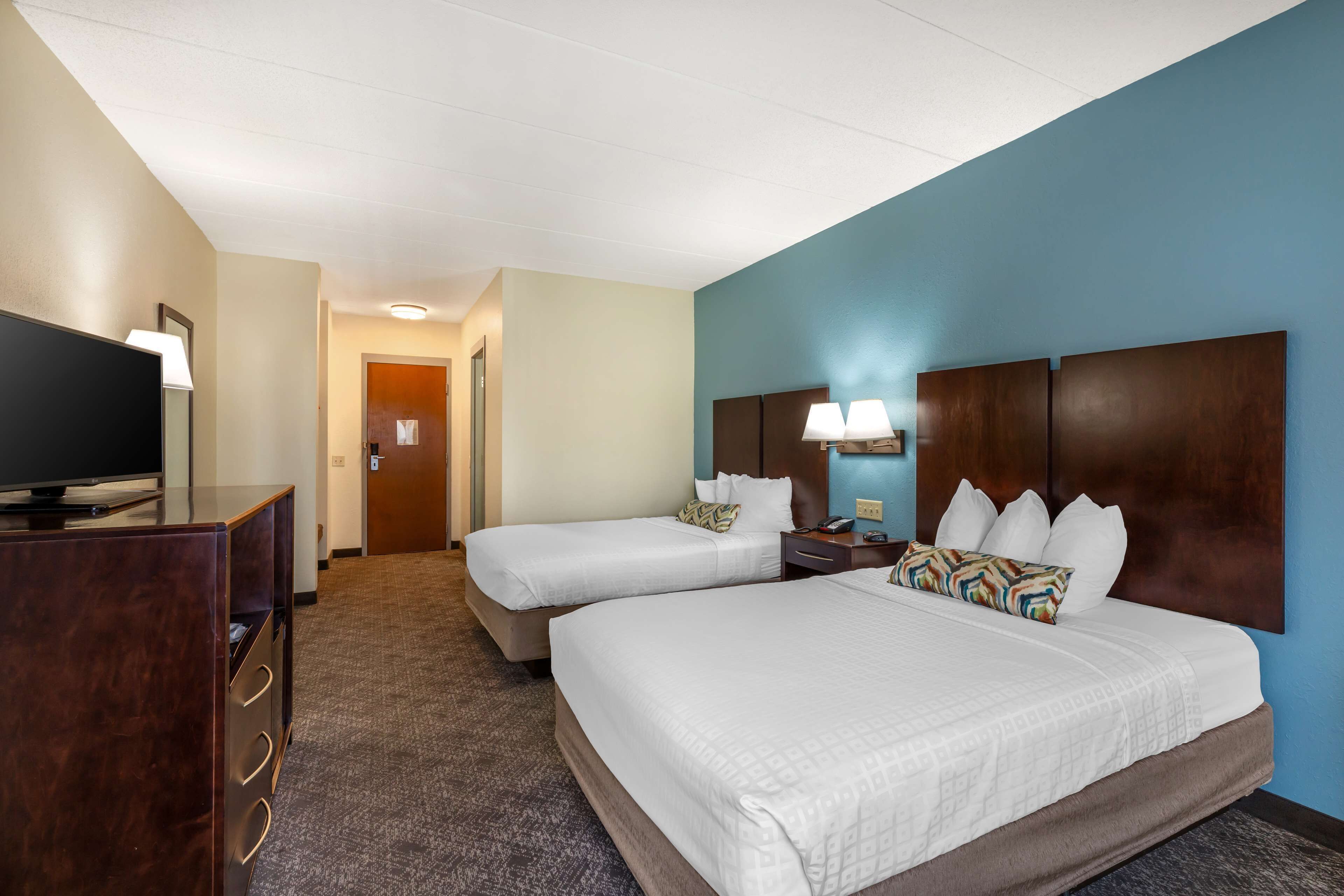 A hotel room with two beds, a TV, a desk, and a lamp.