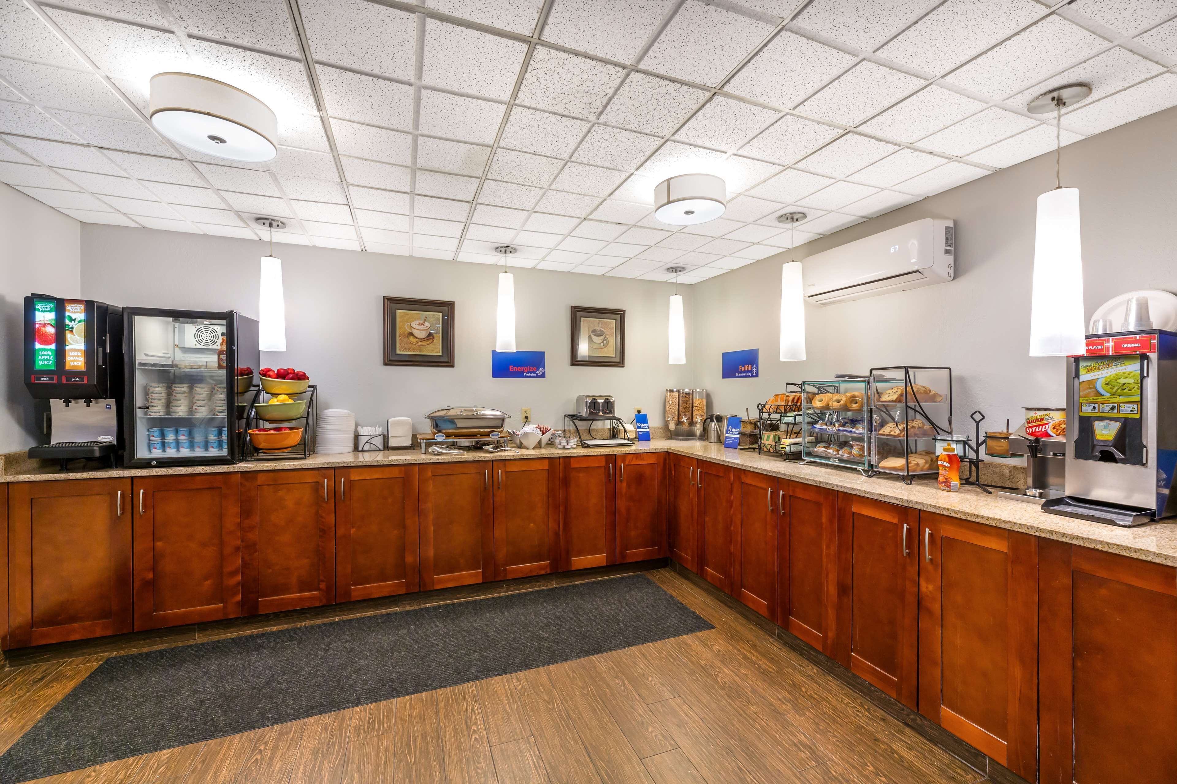 A hotel kitchen with wooden cabinets, a refrigerator, a coffee machine, and a buffet area with various food items.
