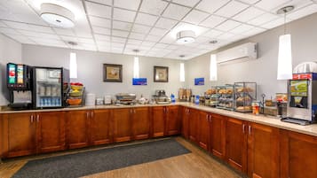 Una cocina de hotel con armarios de madera, un refrigerador, una cafetera y una zona de bufé con diferentes alimentos.