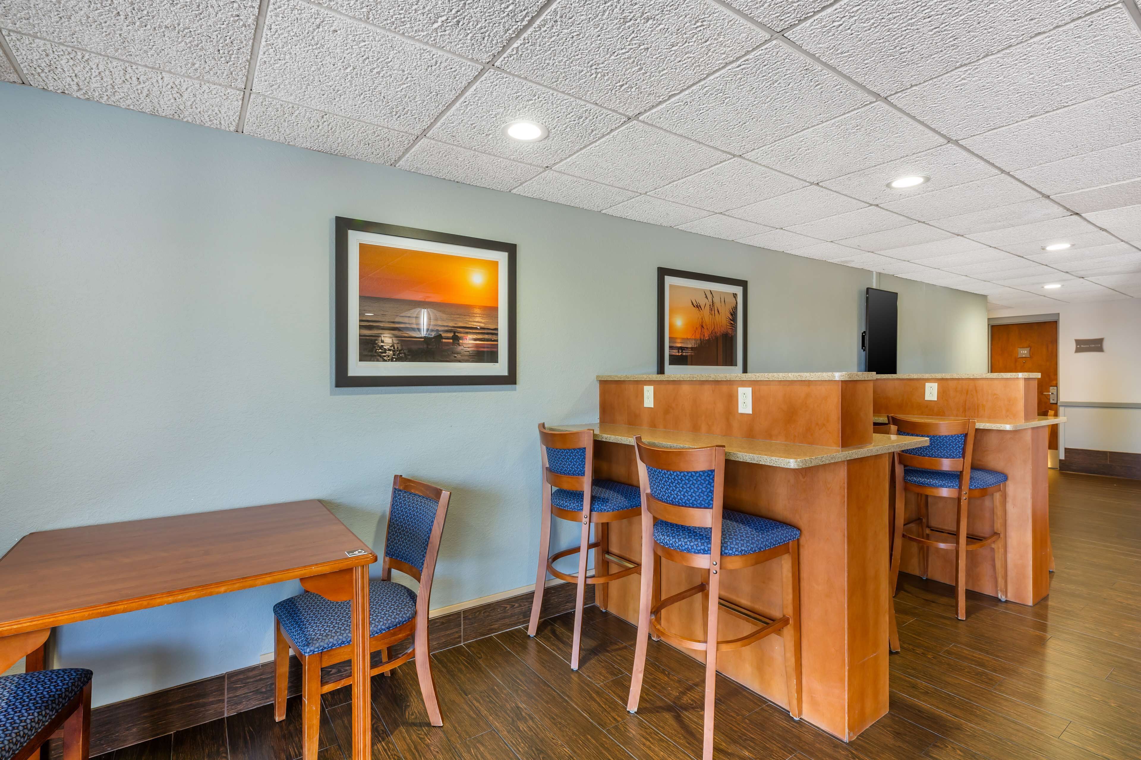 A hotel lobby with a wooden reception desk, bar stools, and framed artwork on the wall.
