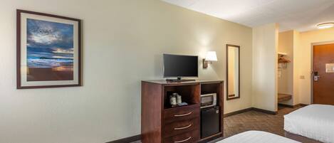 Una habitación de hotel con dos camas, televisión, microondas y un refrigerador pequeño.