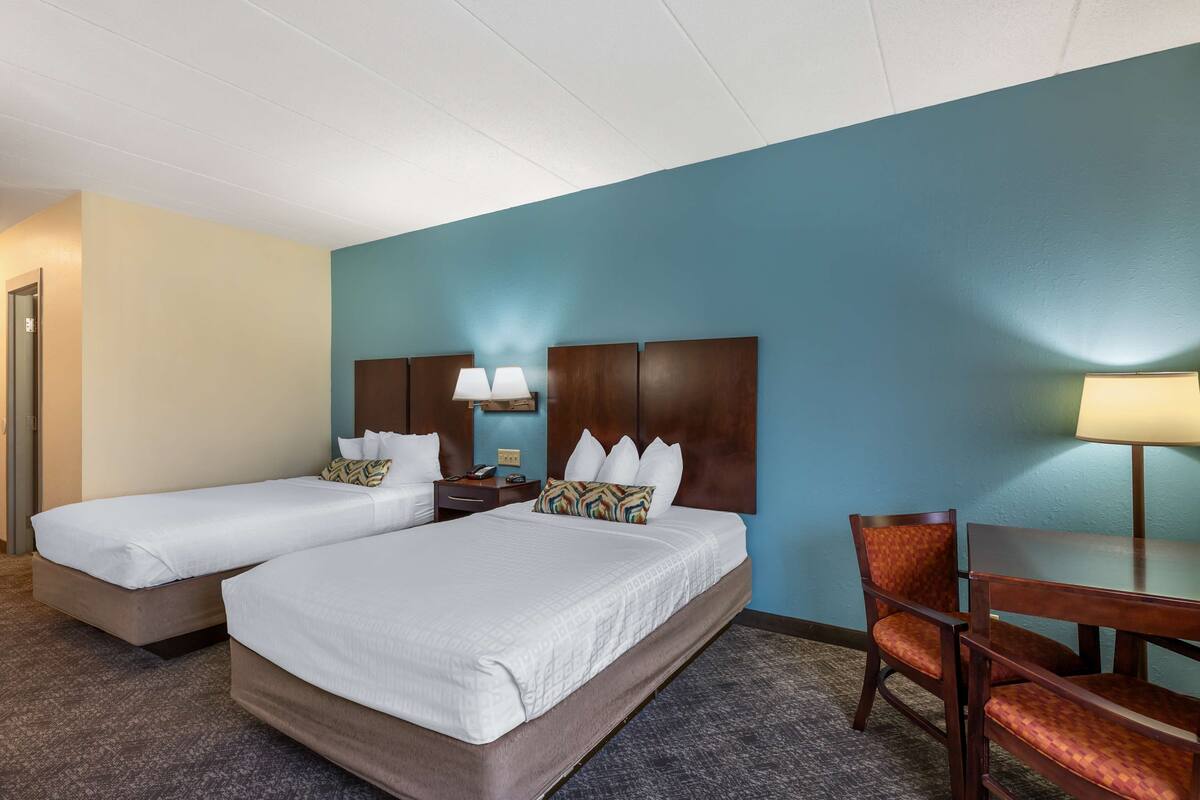 A hotel room with two beds, a desk, and a chair.