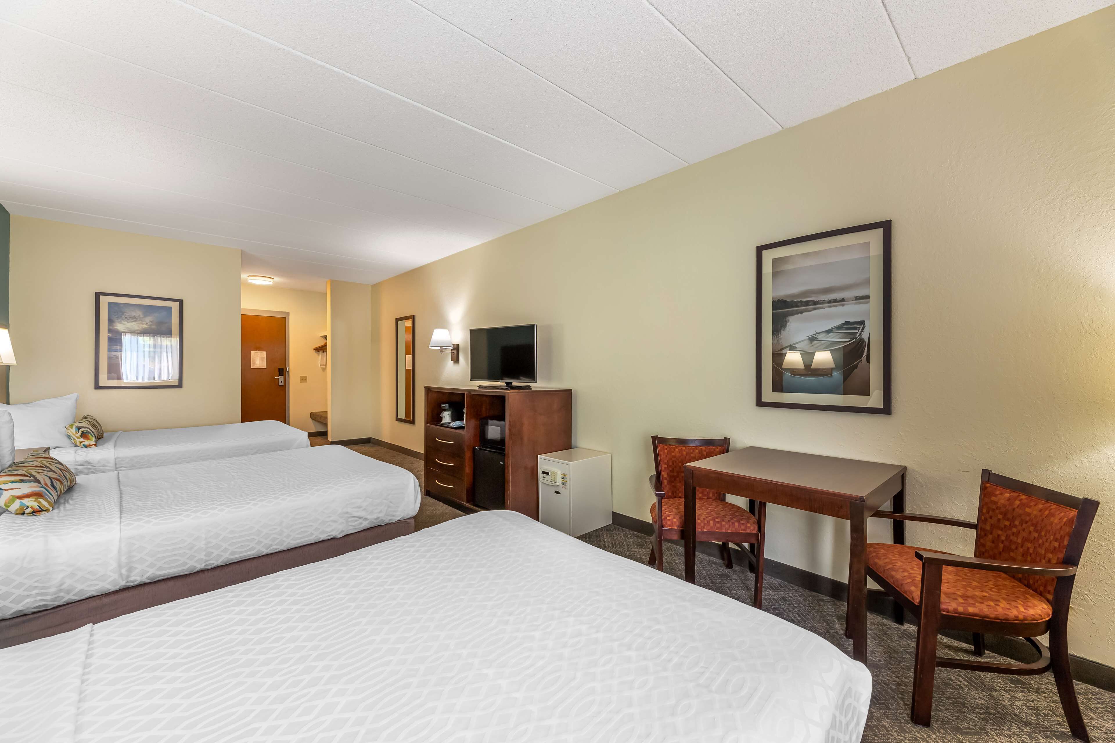 A hotel room with two beds, a desk, a chair, a television, and a small refrigerator.