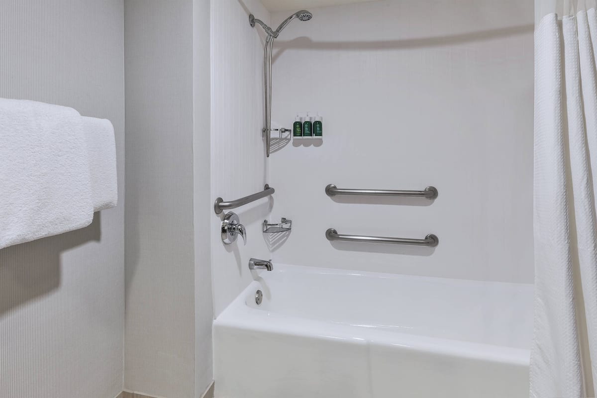Een badkamer met een witte badkuip, handgrepen, een douchekop en een handdoekhouder.