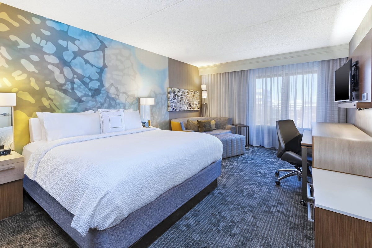Een hotelkamer met een groot bed, een bureau, een stoel, een televisie en een schilderij aan de muur.