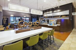 A modern cafe with a long counter, green chairs, and a menu board. - Courtyard by Marriott Secaucus Meadowlands (Secaucus)
