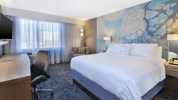 Een hotelkamer met een groot bed, een bureau, een stoel, een televisie en een raam met gordijnen.